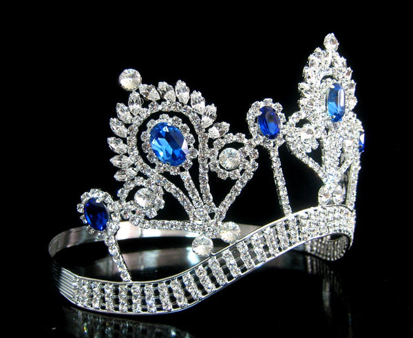An ornate silver tiara crown embellished with sparkling clear crystals and vibrant blue gemstones, displayed on a reflective black surface.